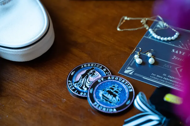 Blue decorative seals and pearl-adorned garters rest on wedding stationery and wooden surface in soft focus.