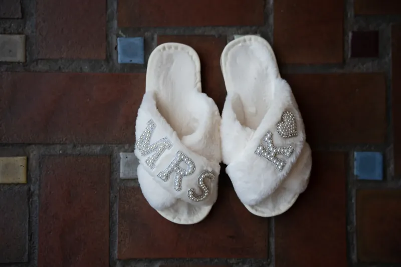 A pair of white embroidered slippers rest on dark wooden flooring at The Treasury on the Plaza.