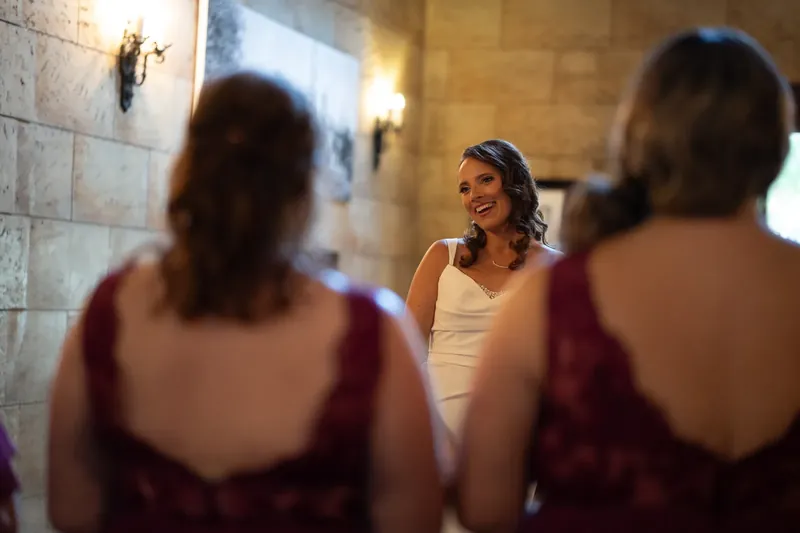 Jessica laughs while surrounded by bridesmaids in burgundy dresses during preparation at The Treasury on the Plaza.