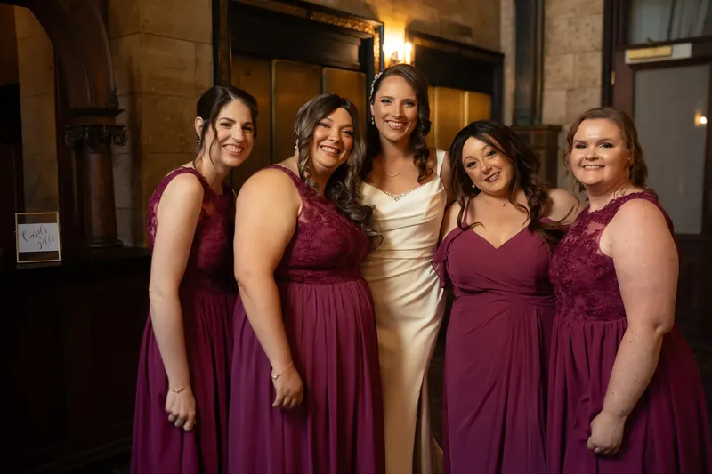 Jessica poses with five bridesmaids in coordinating burgundy gowns inside The Treasury on the Plaza's stone-walled interior.