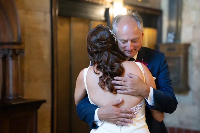 A man in blue embraces Jessica from behind in a candid moment indoors.