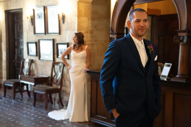John in a navy suit and Jessica in a white gown stand inside the historic stone venue during their first look.