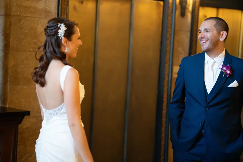 John smiles at Jessica, who wears a backless white dress with a white flower in her hair.