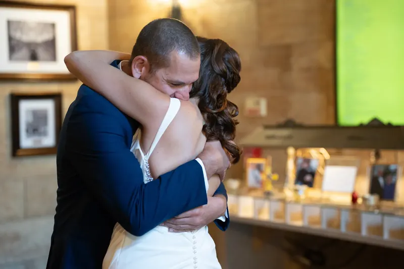 Jessica and John embrace tightly, their foreheads nearly touching, inside the stone-walled reception space.
