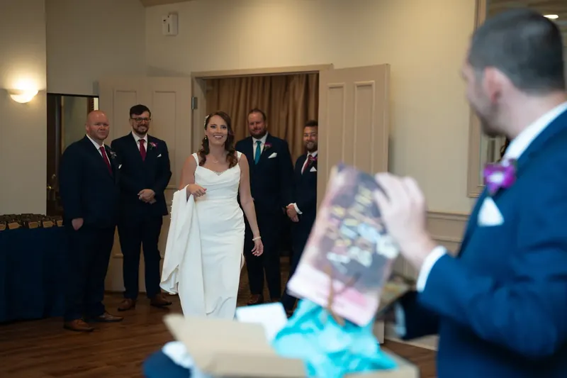 Jessica walks through an indoor room in her white dress, surrounded by men in navy suits at The Treasury on the Plaza.