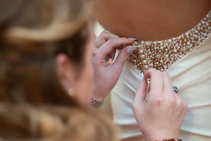 Jessica's hands adjust her pearl-beaded gown straps at The Treasury on the Plaza.