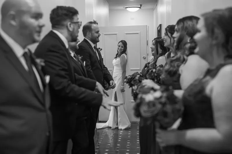 Jessica and John stand together during their ceremony surrounded by guests in formal attire.