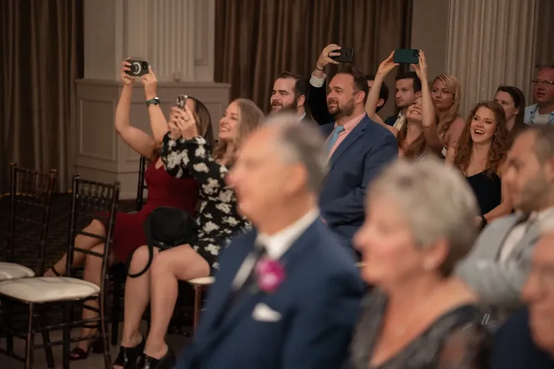 Guests raise their phones and glasses to celebrate as the couple moves through the reception hall.
