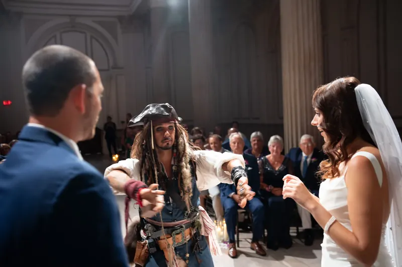 John and Jessica face the pirate character during a playful interaction, with guests visible behind them in formal attire.