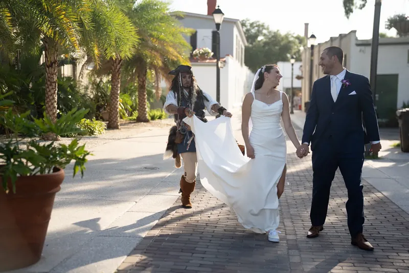 Jessica and John walk hand-in-hand down a sunny brick street, her train flowing behind them.
