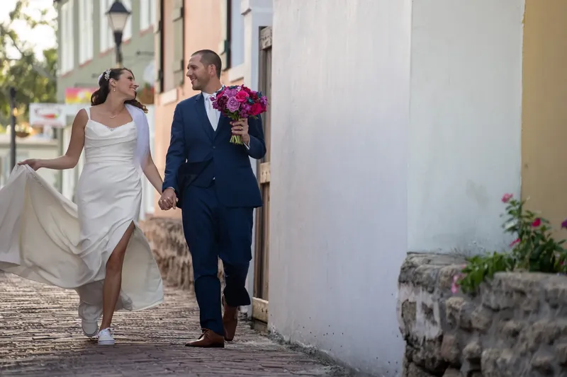 Jessica and John walk together along a narrow brick walkway with white colonial buildings framing the scene.