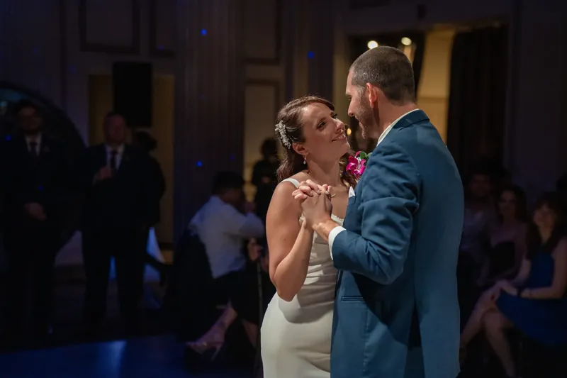 Jessica and John embrace during their first dance, their faces close together as the venue's blue lighting surrounds them.