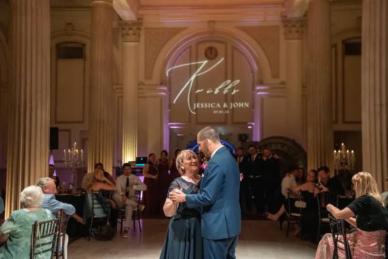 Jessica and John dance together under ornate columns and arches at The Treasury on the Plaza, with guests seated around them.