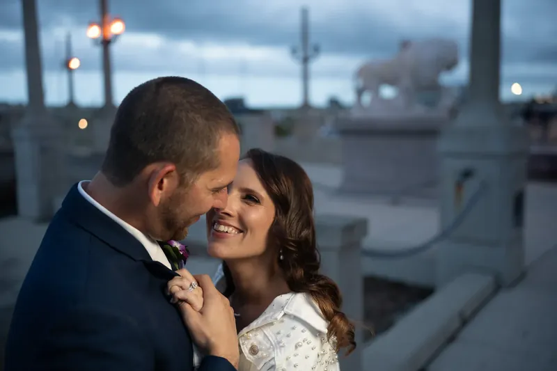 Jessica and John embrace at the St. Augustine Bayfront with waterfront buildings and evening light behind them.