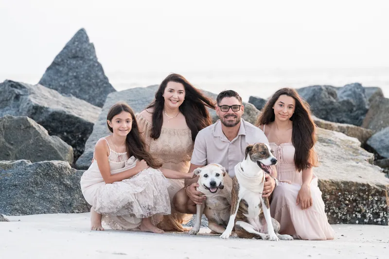 Jessica's family of five sits together on the sand at Vilano Beach, with two dogs, wearing neutral-toned dresses against