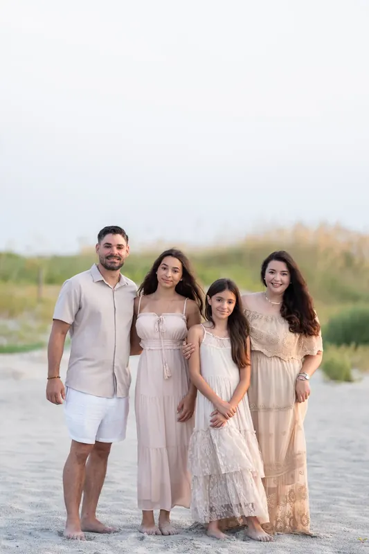 Jessica and three others stand together on sand in neutral-toned clothing, with green marshland visible beyond.