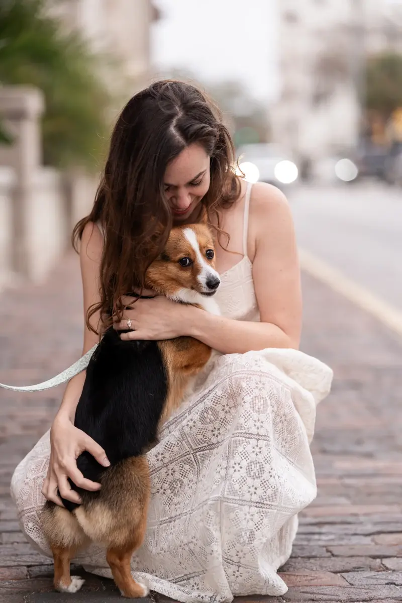 Jillian kneeling on brick street hugging Bonnald the corgi