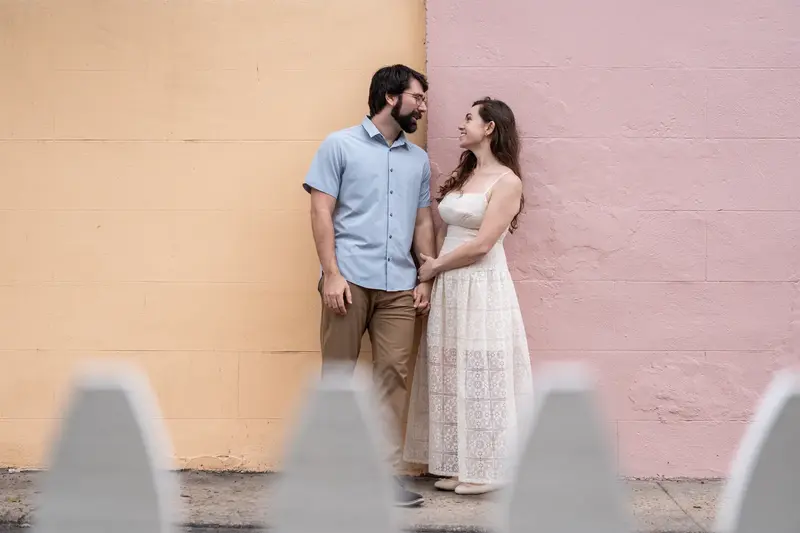 Jillian and Jason holding hands in front of colorful yellow and pink wall
