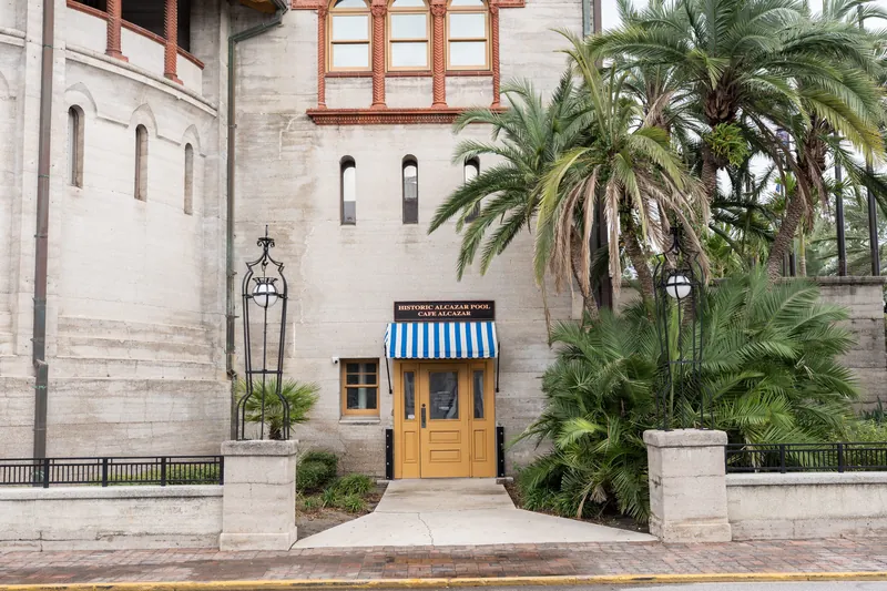 Lightner Museum's classical facade features a yellow door with blue striped awning, flanked by palm trees and stone columns.