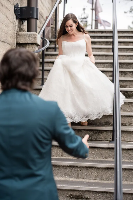 A person in a white gown descends stone steps while someone in teal watches from below at Lightner Museum.