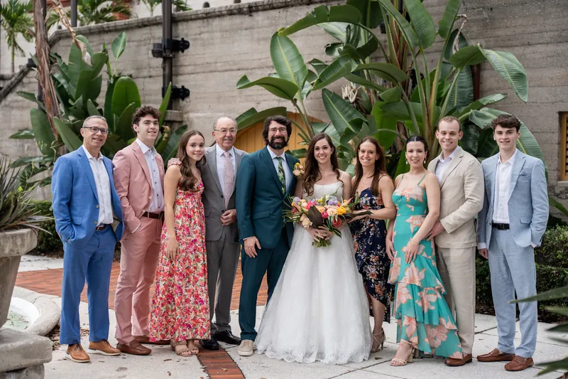 Wedding party of ten stands in a line on a brick pathway, framed by oversized green foliage at Lightner Museum, St. Augustine.