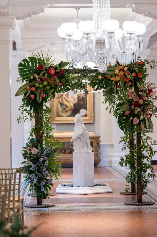 Ornate archway draped in cascading greenery and florals frames a classical statue indoors at Lightner Museum, St. Augustine.