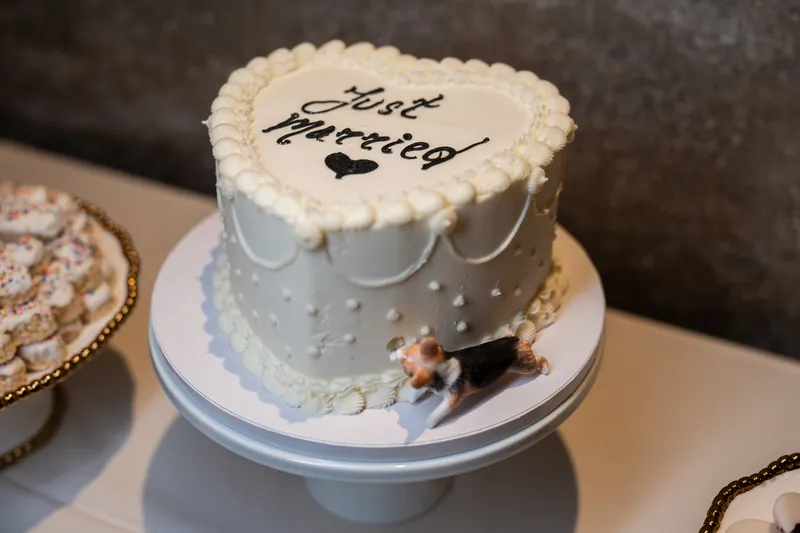 A tiered wedding cake with beaded piping reads "Just Married" in script, topped with a small figurine of a couple.