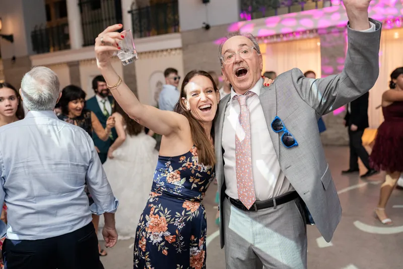Two guests dance with arms raised, laughing and celebrating on the dance floor at the Lightner Museum reception.