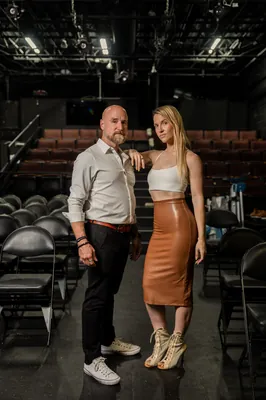 Couple poses on the theater stage at Limelight Theatre, the woman resting her hand on the man's shoulder with rows of seats