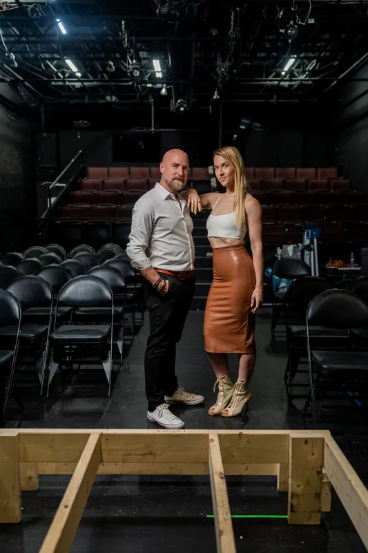 Couple stands on the stage at Limelight Theatre with wooden stage construction visible in the foreground and empty theater