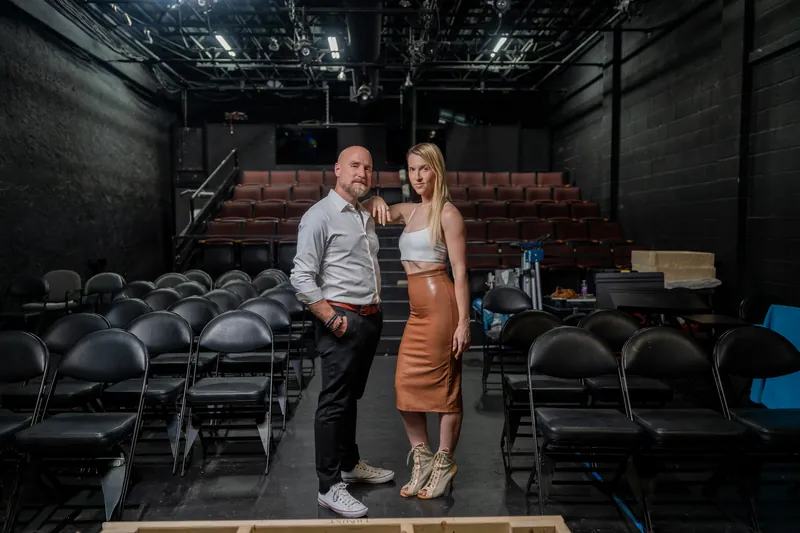 Couple poses together on the stage at Limelight Theatre, the darkened theater interior and seating rows stretching out behind