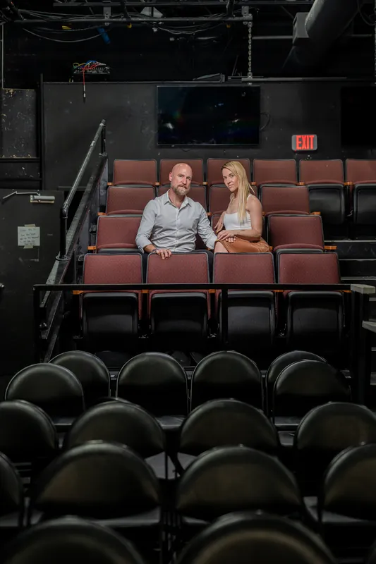 Inside Limelight Theatre's auditorium, a couple sits in the middle section of burgundy seats surrounded by empty black seats
