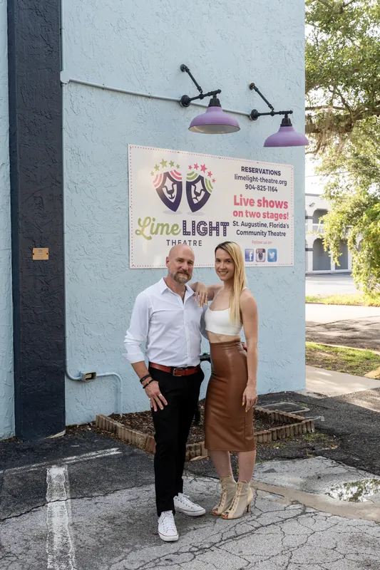 Jimmy and a woman stand outside Limelight Theatre in St. Augustine, posing beside a vintage-style wall lamp and promotional