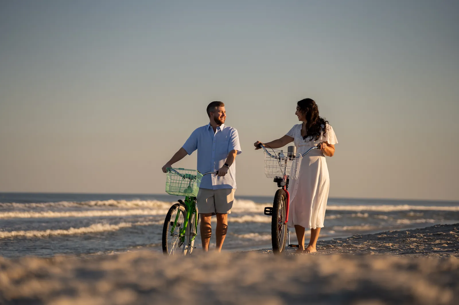 Joanne and Zack standing with their bikes on Jacksonville Beach at sunset