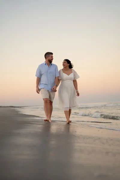 Couple walking bicycles together on beach at sunset