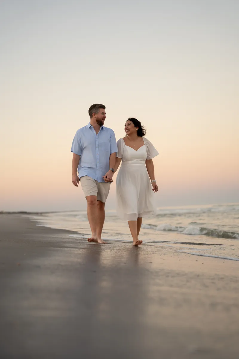 Couple walking bicycles together on beach at sunset