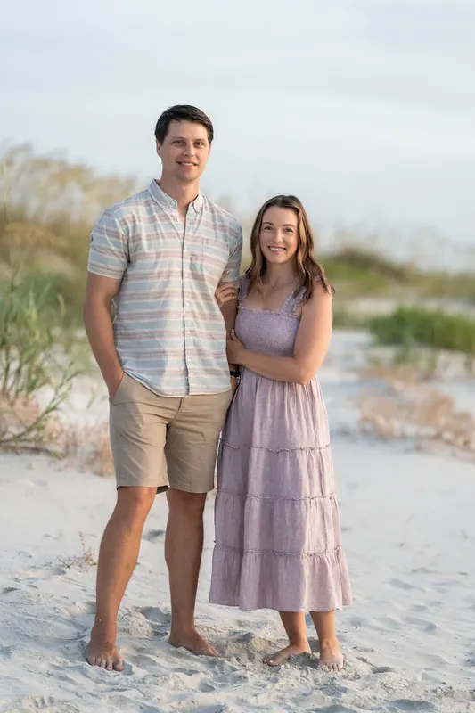 Jourdan and partner stand together on the sand with dune grass behind them at St. Augustine Beach.