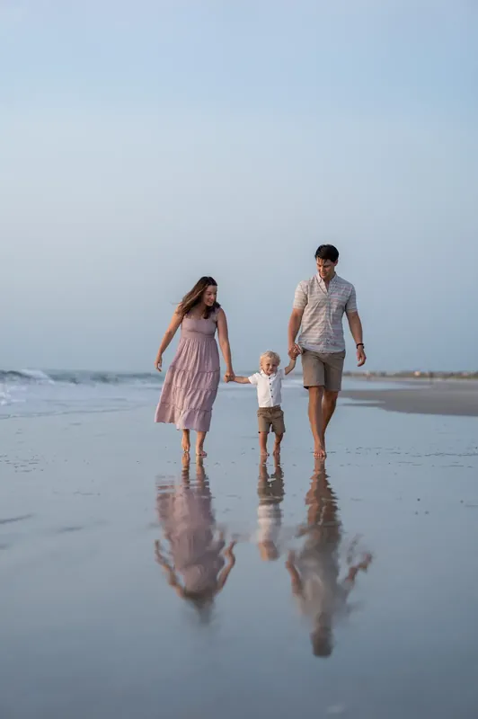 Two adults and a toddler walk together across reflective wet sand at St. Augustine Beach toward the ocean.