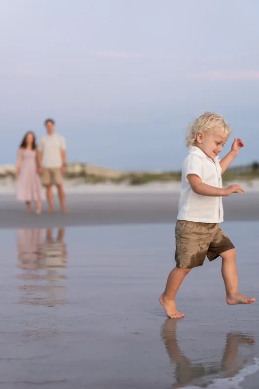Child races across the packed sand as the family looks on in the distance at St. Augustine Beach.