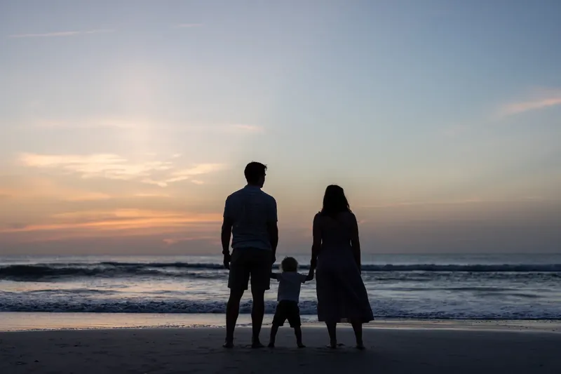 Jourdan, partner, and child stand silhouetted against the sunset over the ocean at St. Augustine Beach.
