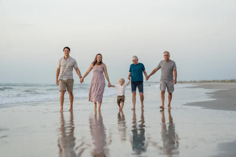 Five people stand together in the shallow waves at St. Augustine Beach at dusk, holding hands and smiling at the camera.