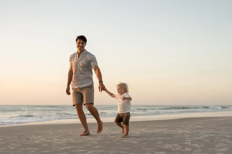Jourdan walks barefoot along the shoreline with their toddler at St. Augustine Beach.
