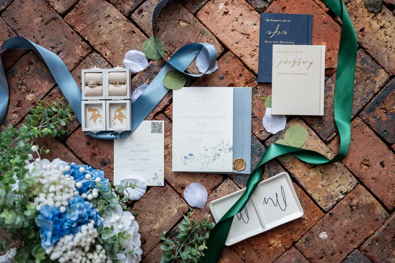 Invitation suite and baby's breath arranged on cork with blue ribbon and floral accents at The White Room.