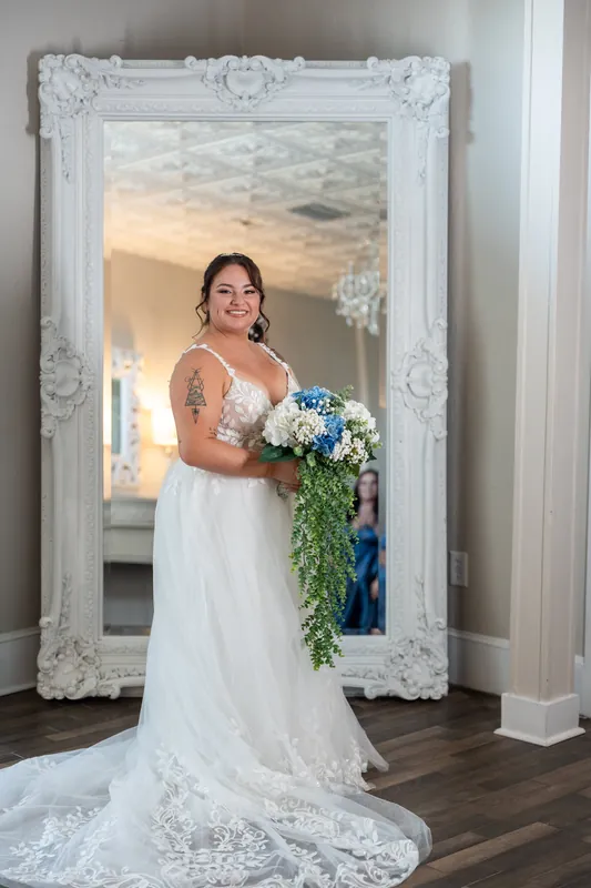 Person in white gown holds cascading bouquet before ornate mirror at The White Room.