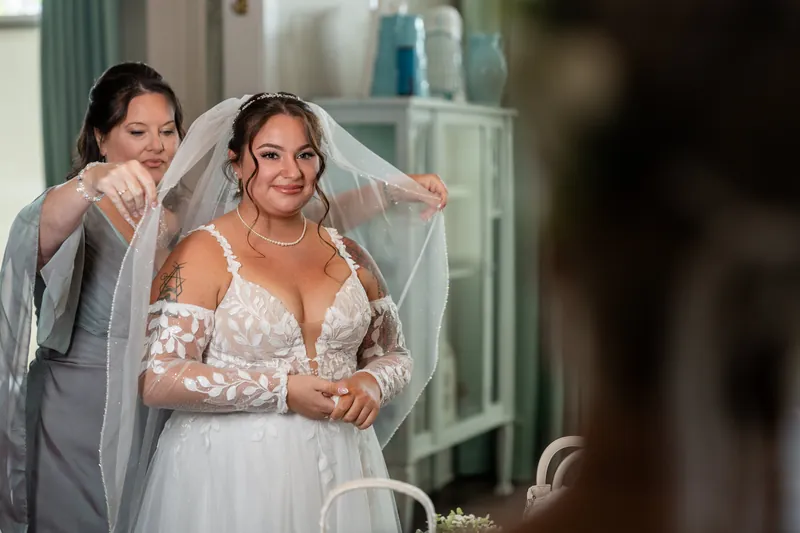 Julia and William stand at the altar as a person adjusts Julia's veil in The White Room's bright chapel.