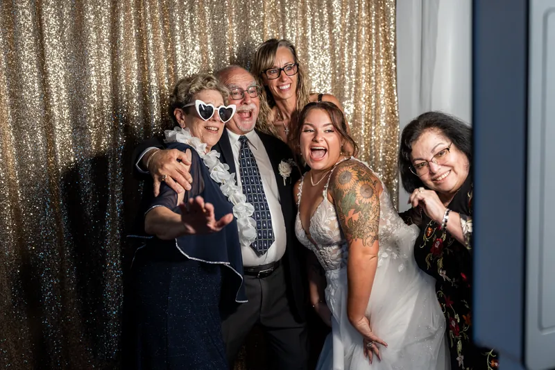 Five people laugh together against a gold sequin backdrop, striking playful poses.