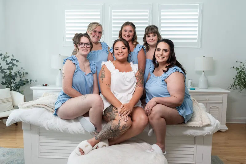 Six people in coordinating blue and white outfits sit together on a bed, smiling at the camera.