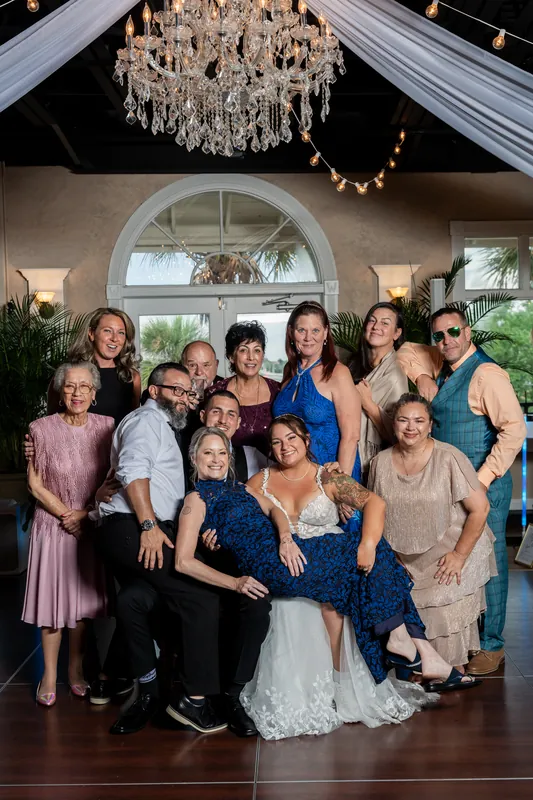 A multi-generational family group stands together on the dance floor, with one person in a white gown in the center.