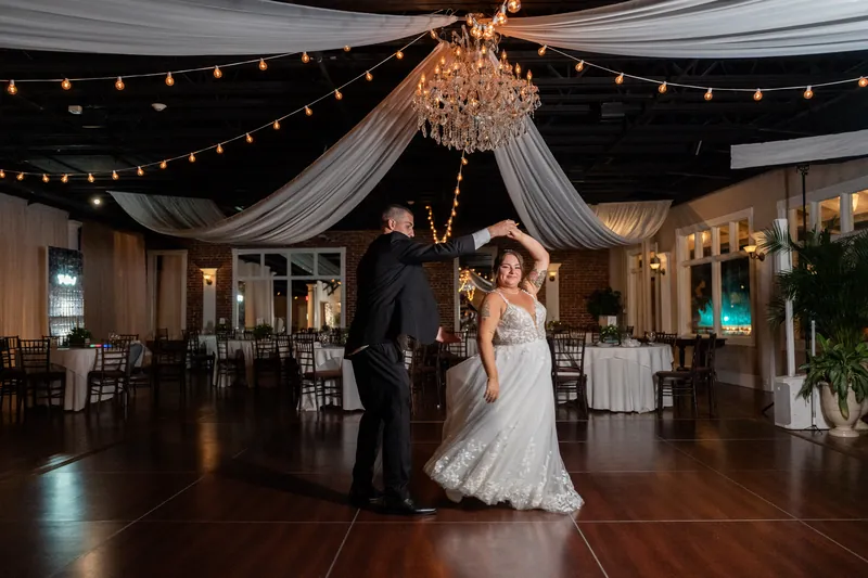 Two people dance beneath a draped ceiling with a crystal chandelier and string lights at The White Room.