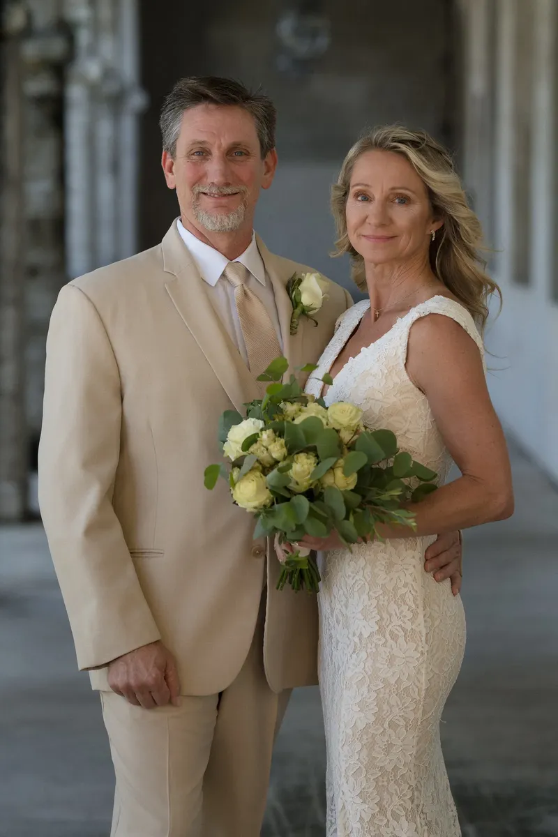 Couple portrait together with groom in tan suit and bride holding bouquet